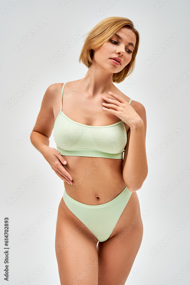 Sexy young blonde woman with natural makeup in light green lingerie touching chest and looking away while standing isolated on grey, self-acceptance and body positive concept Sexy young blonde woman with natural makeup in light green lingerie touching chest and looking away while standing isolated on grey, self-acceptance and body positive concept