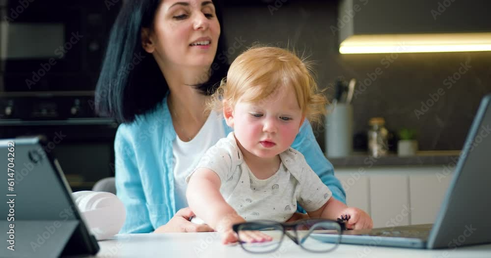 Remote work woman and child care concept where good-looking confident loving mother holding his small son on knees during explanation of report with statistics through video chat at home Remote work woman and child care concept where good-looking confident loving mother holding his small son on knees during explanation of report with statistics through video chat at home