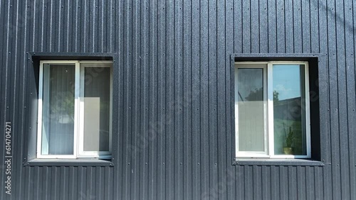 Black metal facade of house, two plastic windows.