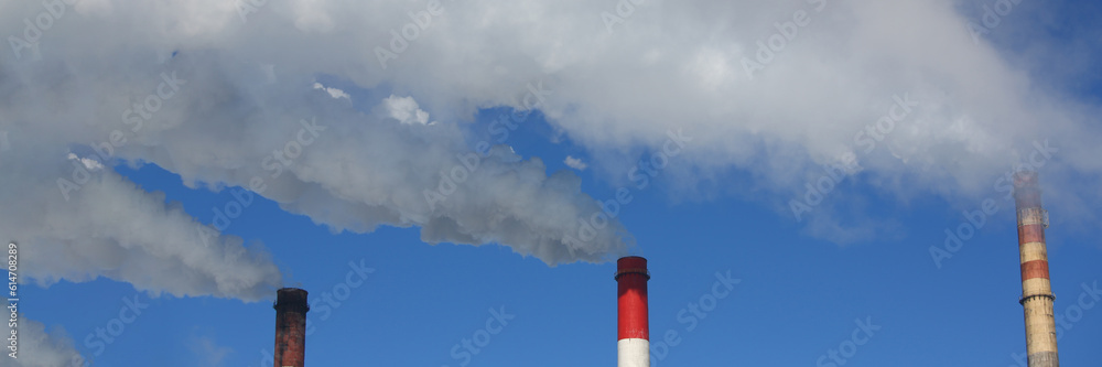 Three pipes of thermal power plant with steam and smoke against blue sky during heating season. Work CHP concept Three pipes of thermal power plant with steam and smoke against blue sky during heating season. Work CHP concept