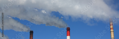Three pipes of thermal power plant with steam and smoke against blue sky during heating season. Work CHP concept