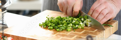 ook cuts green onions on board in kitchen. Cooking vegetable salad concept photo