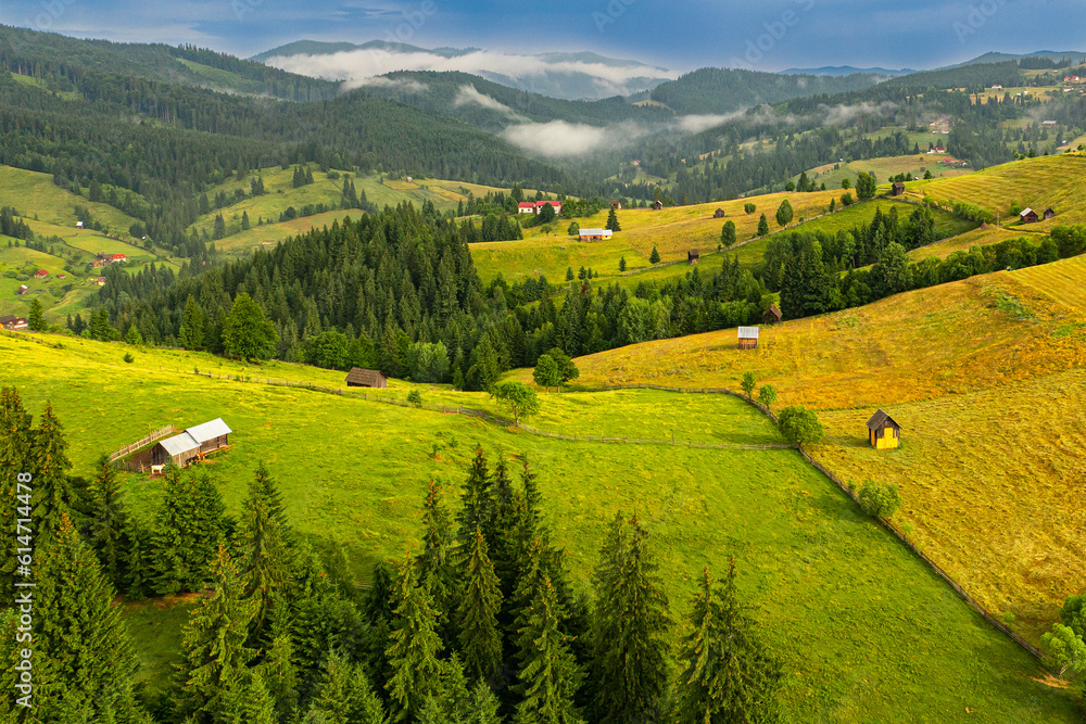 Obraz premium Travel to Bucovina, Romania. Aerial view over a farm with haystacks in a beautiful village mountain area from Suceava.