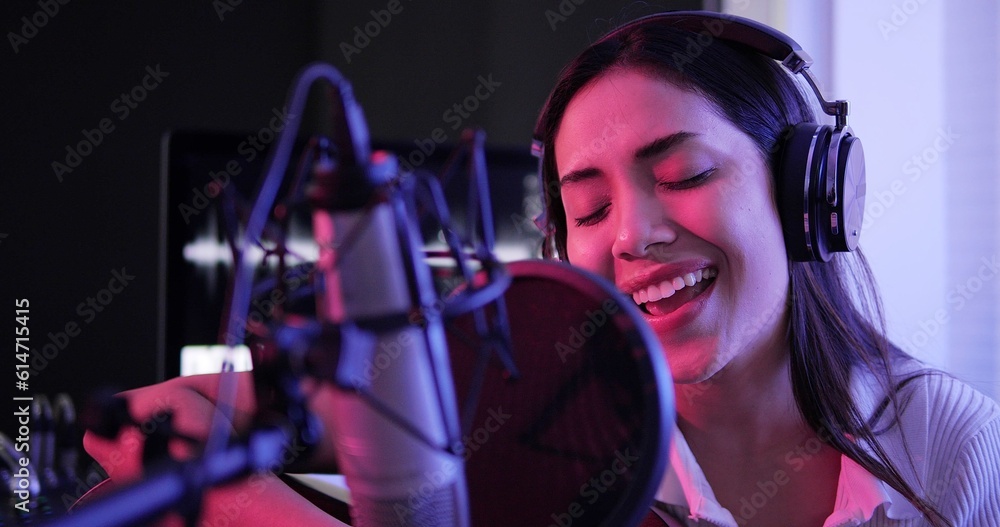 Young asian woman artist singing song at music studio. Woman singer wearing headphones using microphone singing a song in recording neon studio Young asian woman artist singing song at music studio. Woman singer wearing headphones using microphone singing a song in recording neon studio