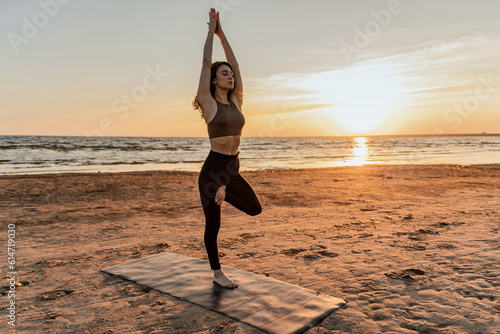 Calm and harmony. Balance and meditation woman training yoga asana outdoors near the lake. The trainer uses an aerobics mat at sunset.