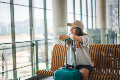 Obraz na płótnie Young cheerful dreamy woman sitting at the airport in the waiting area for departures with a suitcase. Summer travel concept w salonie