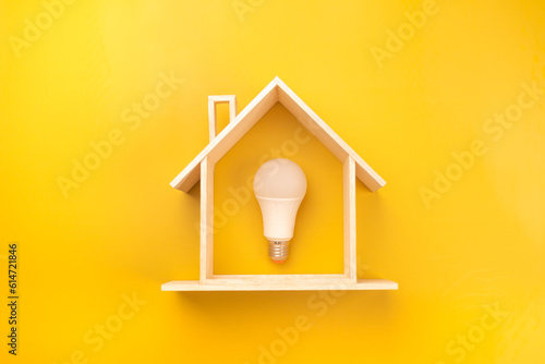 White light bulb in model wooden house on bright yellow background. Energy saving light bulb on yellow background. energy efficient home concept, new home Idea. energy saving concept.