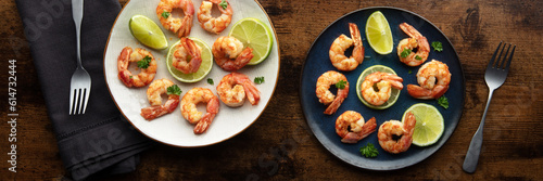 Shrimps panorama. Cooked shrimp, two plates, overhead flat lay shot. With lime and forks, on a rustic wooden background, panoramic banner