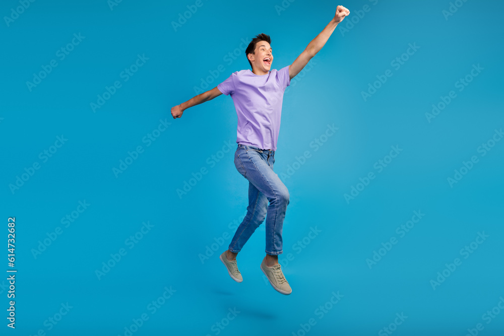 Full length portrait of excited young man in t-shirt jumping motivation safe world isolated over blue background