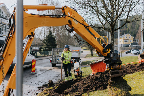 Female road worker and excavator at digging site