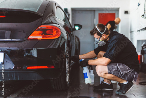 Service man washing car before detailing in workshop.