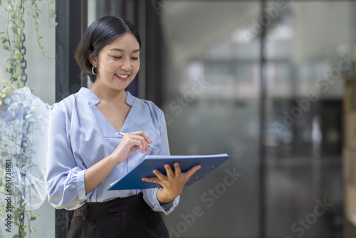 Boring young business Asian woman holding document file and looking at camera stand on a workplace office. © David