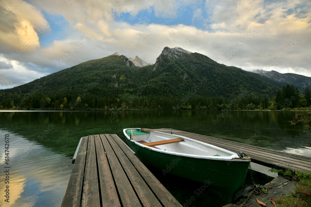 Ein Ruderboot liegt in einer schönen Abendstimmung an um Bootsanleger eines Bergsee und im Hintergrund sind mehrere Berggipfel zu sehen