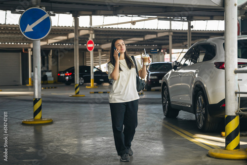 A young woman with coffee talking on the phone in the parking lot. © puhimec
