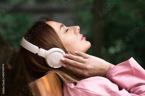 A young beautiful woman listening to music with headphones with her eyes closed on a park bench. Peace  harmony  relaxation and relaxation.