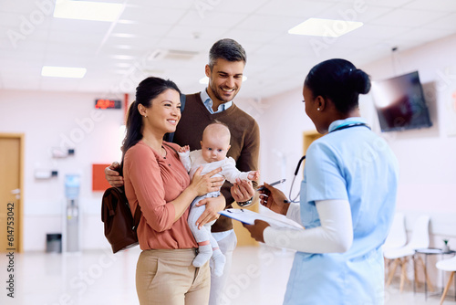 Happy parents with baby talking to black nurse in hallway at pediatric clinic. photo