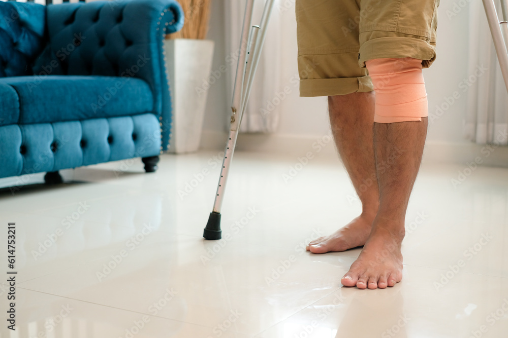Man with knee injury had bandaged his knees and was using crutches learning to walk in the room. Man with knee injury had bandaged his knees and was using crutches learning to walk in the room.