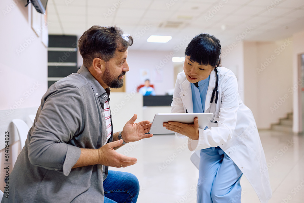 Obraz premium Japanese doctor and her male patient talk while using touchpad at clinic.