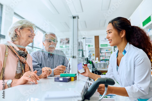 Happy Chinese pharmacist assists her senior customers in buying medicine in pharmacy.