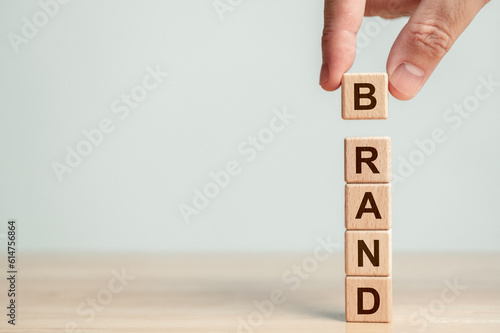 Hand stacking wood cube block with BRAND word on wooden table. Business startup and entrepreneur concept. Marketing