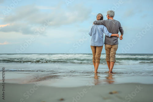 Plan life insurance of happy retirement concepts. Senior couple walking on the beach holding hands at beach sunrise in evening.