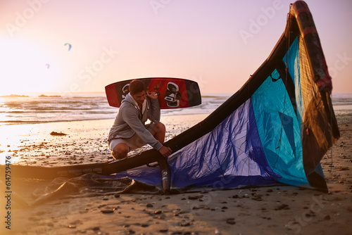 Man with kiteboarding equipment on sunset beach