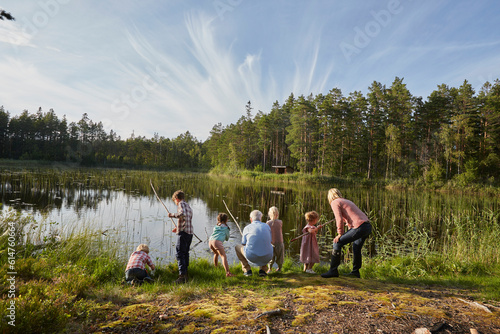 Grandparents and grandchildren fishing at sunny lakeside in woods