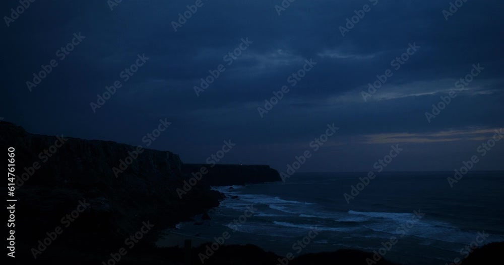 The light of the lighthouse located behind the rocks surrounding the sandy beach. Sea coast at night The light of the lighthouse located behind the rocks surrounding the sandy beach. Sea coast at night