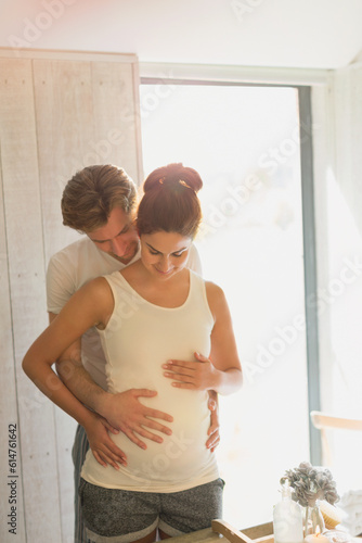 Pregnant couple holding stomach in sunny bathroom