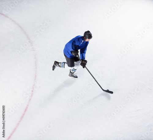 Photography Hockey player in blue uniform skating with puck on ice