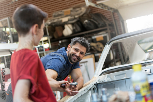 Smiling father taking tool from son in auto repair shop