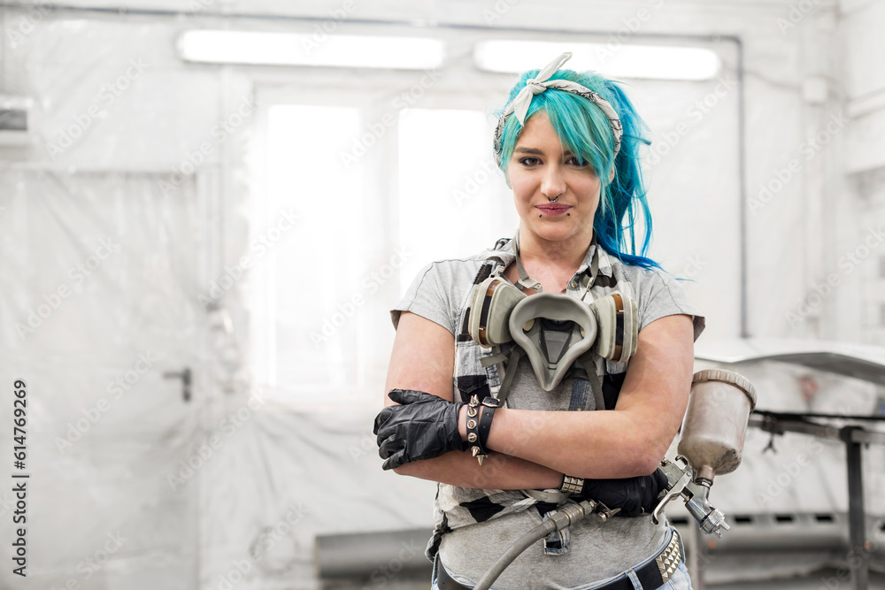 Portrait confident young woman blue hair paint gun in auto body shop