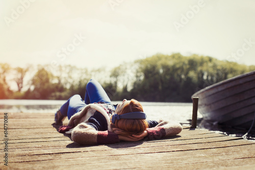 Fototapeta Woman relaxing laying on dock listening to music headphones at sunny lakeside