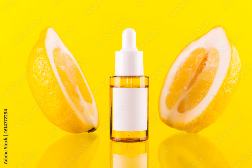Bottle with lemon essential oil with half of lemon slices on yellow background. Cosmetic citrus oil or serum. Natural medicine concept. Aromatherapy and advertising concept. Bottle with lemon essential oil with half of lemon slices on yellow background. Cosmetic citrus oil or serum. Natural medicine concept. Aromatherapy and advertising concept.