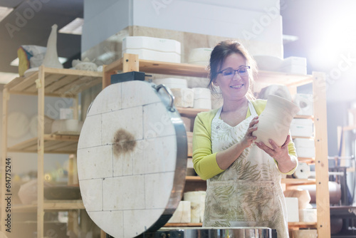 Quadro su tela Smiling mature woman placing pottery vase in kiln in studio