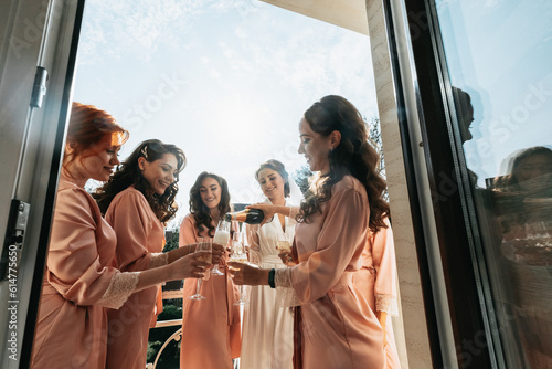 Canvas Print Young bridesmaids are having fun and smiling in pink silk robes drinking champagne at the bride's gazebo