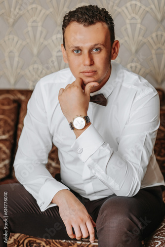 Close-up of a fashionable image of a luxury watch in the city. Detail of a business man's body. Man's hand in brown pants pocket close-up on gray background.A man wearing brown pants and a white shirt