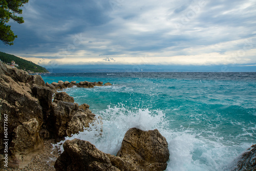 The ocean wave is hitting a rocky seashore. Stormy turqouse blue sea by the promenade in Moscenicka Draga, Croatia. Sea water splash and cloudy sky. Storm and wind. Top view from above.