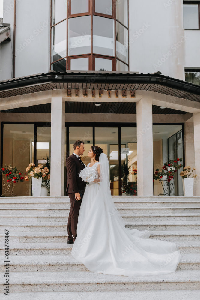 Obraz premium Groom and bride walking outdoors near a posh hotel. A long train of dress on the steps