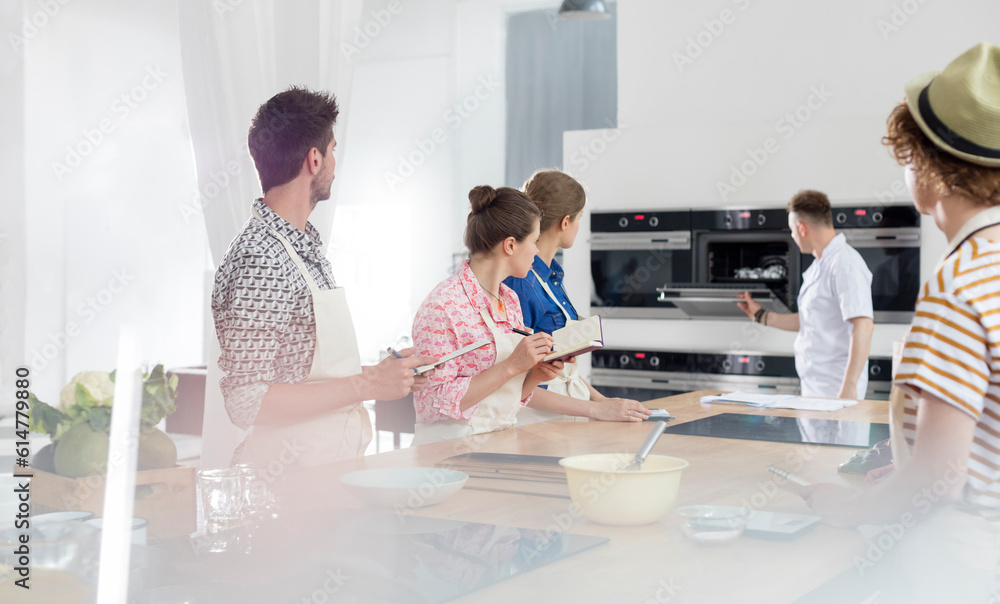 Fototapeta premium Students taking notes watching chef teacher at oven in cooking class kitchen