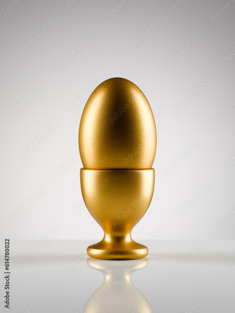 Golden egg in egg cup holder against white background Golden egg in egg cup holder against white background
