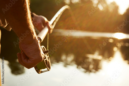 Close up senior man fly fishing at sunny lake
