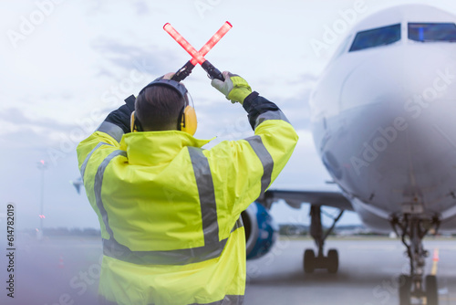 Fotografie Air traffic controller guiding airplane with wand lights on tarmac
