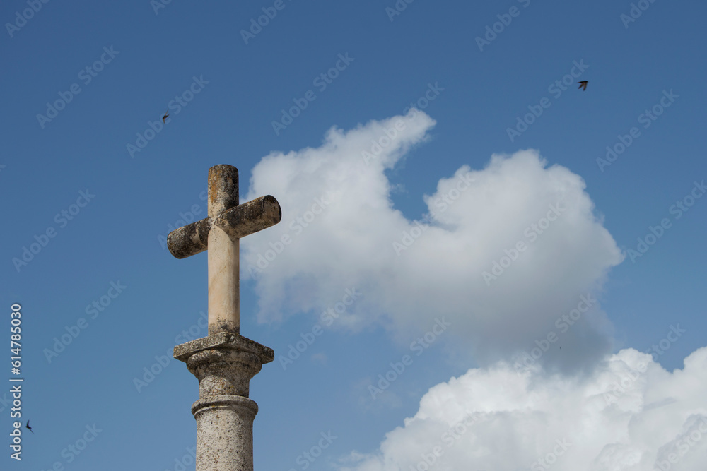 stone cross on sky with clouds and three birds flying around it