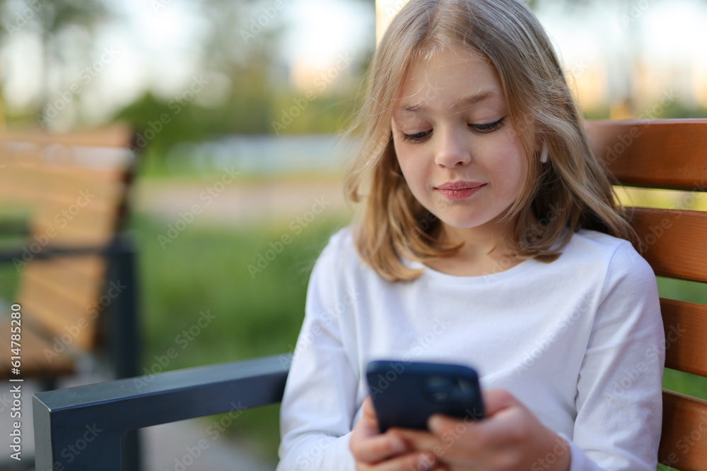 Girl child with a smartphone in her hands on a bench in the park. Girl child with a smartphone in her hands on a bench in the park.