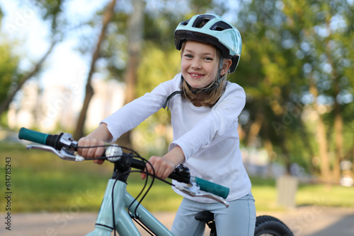 Smiling child girl in a protective helmet on a bicycle in the park.