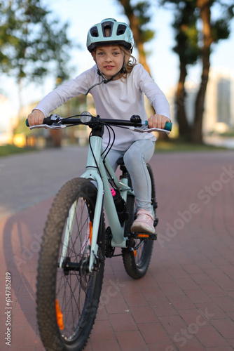 A girl in a protective helmet rides a bicycle on a cycle path.