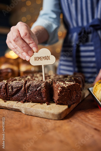 Sales Assistant In Bakery Putting Homemade Label Into Freshly Baked Baked Chocolate Brownies