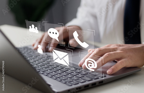 Businessman use laptop for customer service. Please contact us if you are looking for a people connection. Businessman has email, phone, address, and chat message symbols on his smartphone..