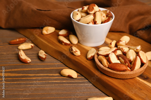 Board with bowl and plate of tasty Brazil nuts on wooden background
